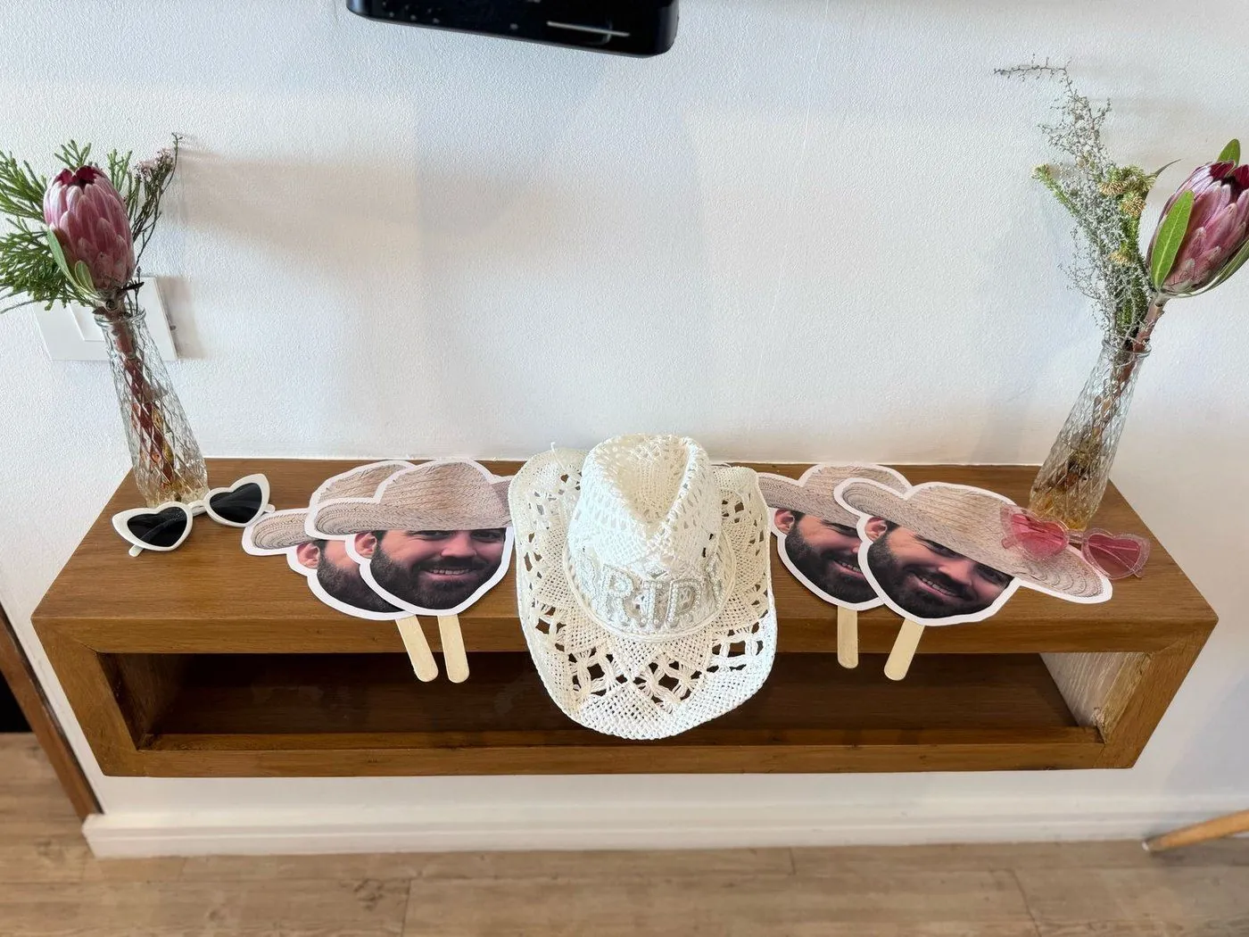 Bachelorette flatlay with king protea blooms, a BRIDE hat, heart sunglasses and custom face fans