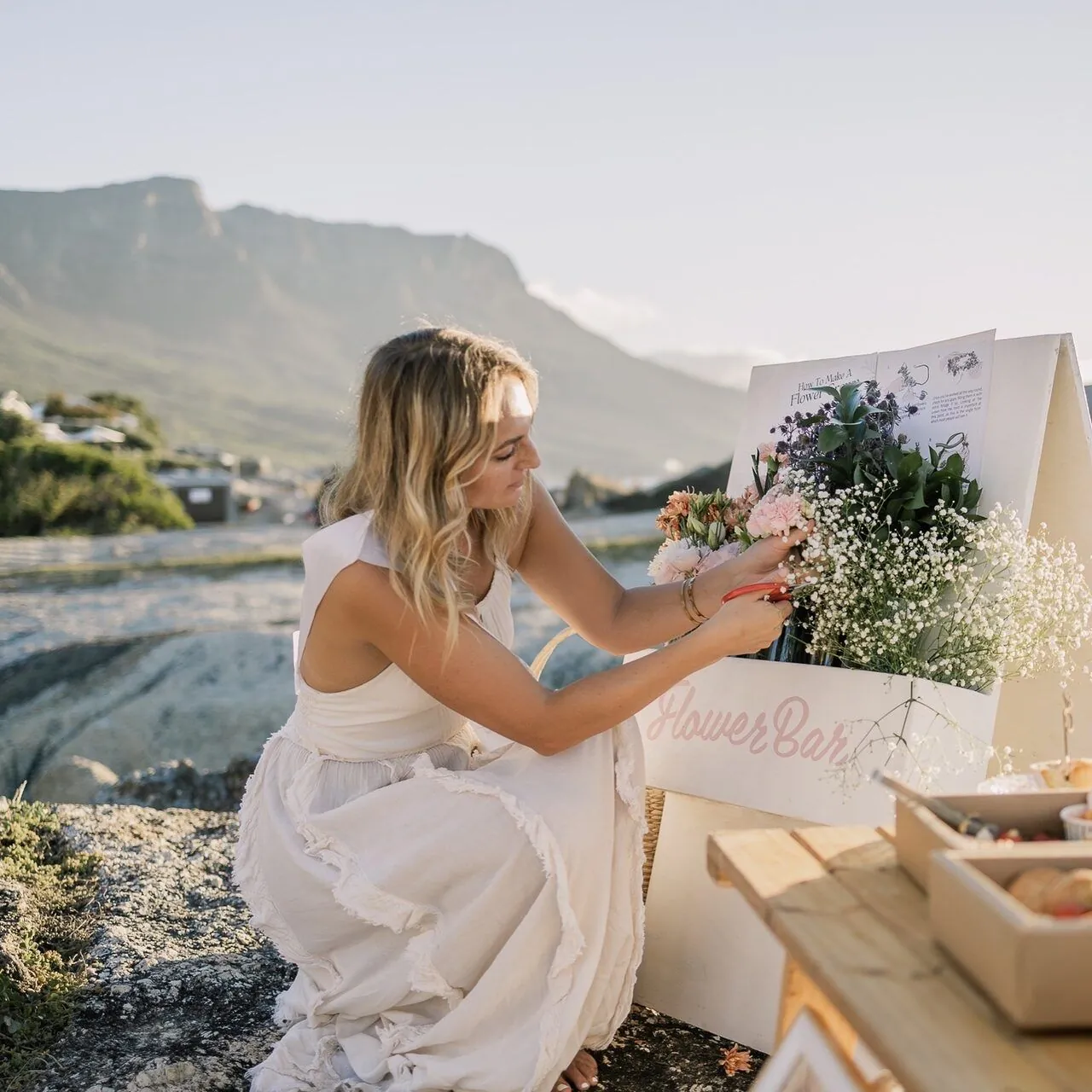 Bride styling a beach flower bar with Table Mountain behind, Cape Town