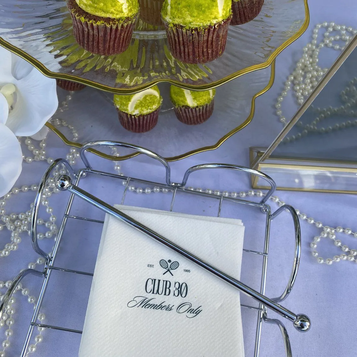 Tennis-ball cupcakes and a Club 30 tennis napkin styled with pearls at a bachelorette