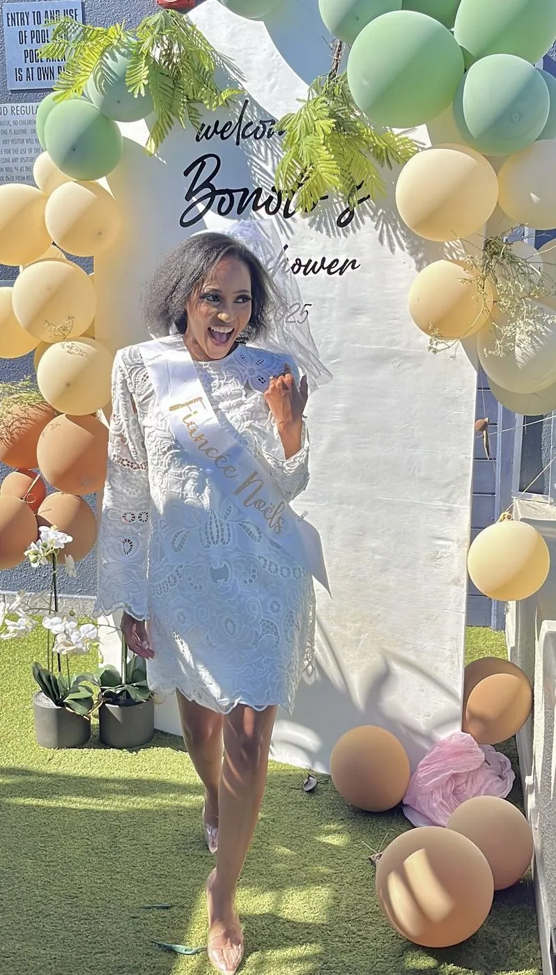 Bride-to-be in a Fiancée sash laughing in front of a sage and cream balloon arch at a rooftop bridal shower, Cape Town