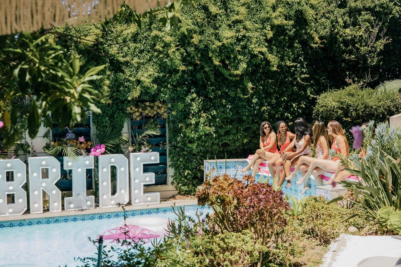 Friends by the pool beside a glowing BRIDE marquee in a lush Cape Town garden
