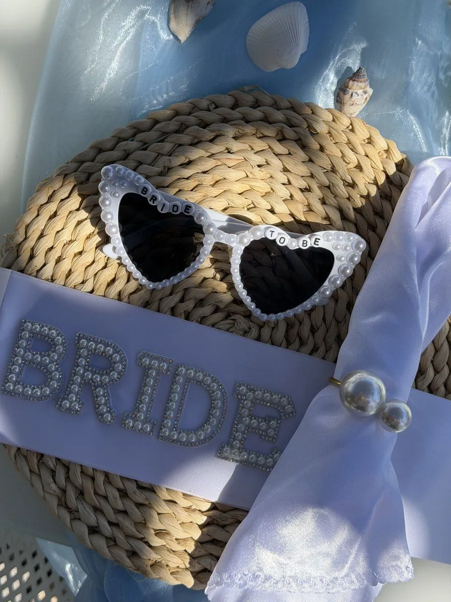 Pearl BRIDE sash and heart-shaped bride-to-be sunglasses styled on a rattan bag