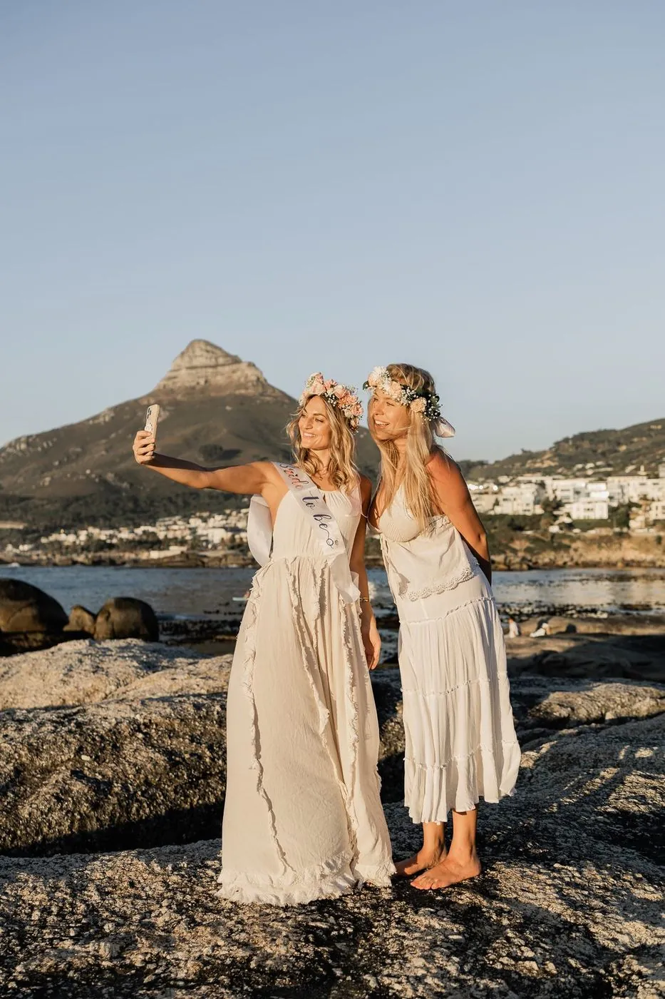 Bride-to-be in a Bride to Be sash taking a selfie with a friend in floral crowns below Lion's Head, Cape Town