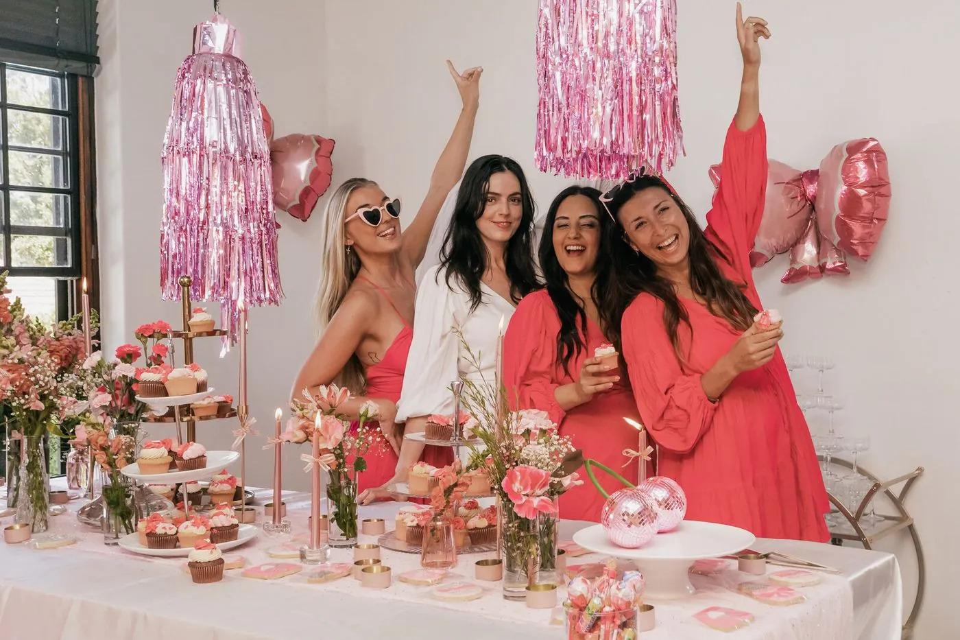 Friends celebrating at a pink dessert table with cupcakes and florals