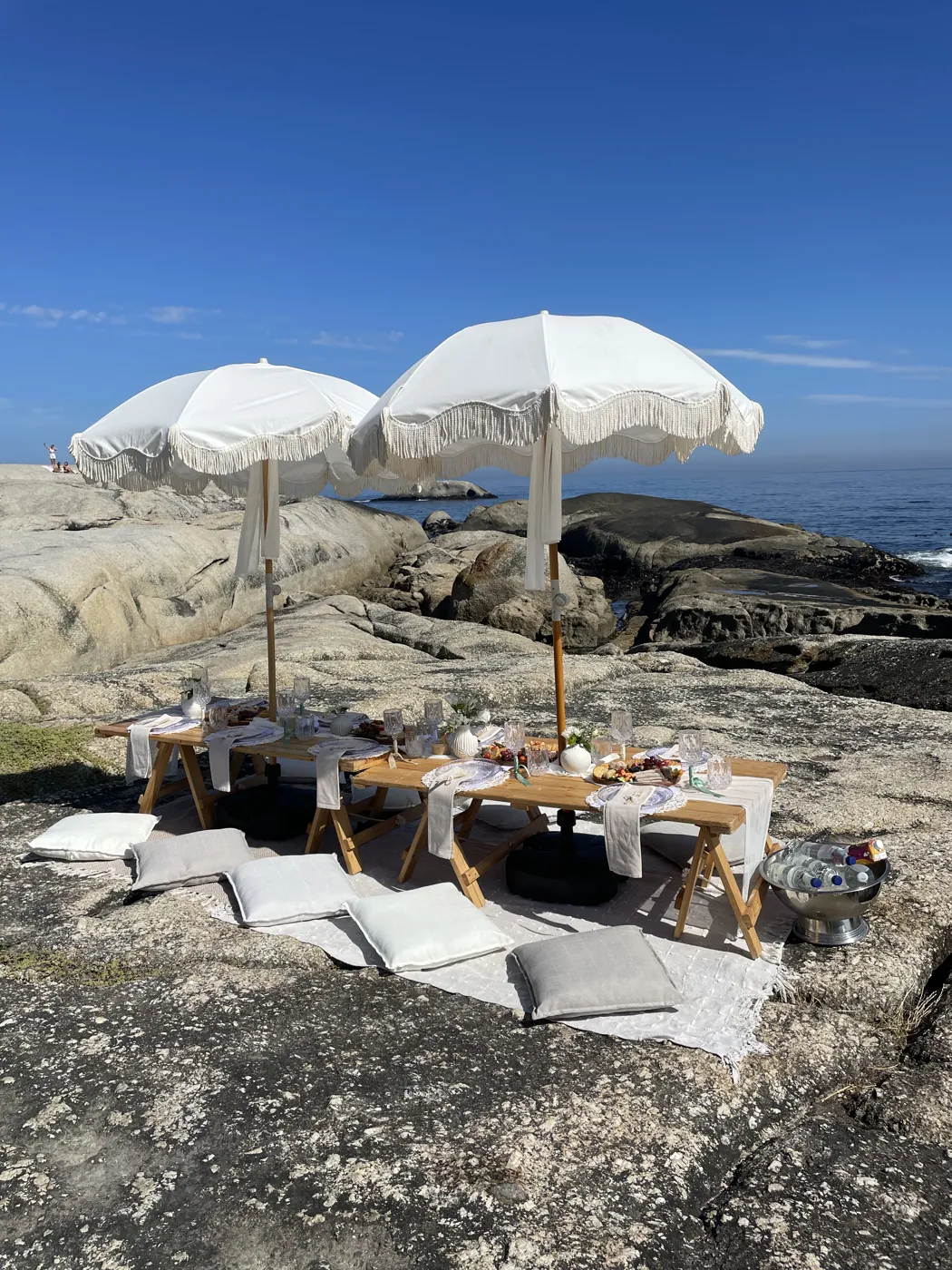 Styled beach picnic with white parasols and low table on the rocks at a Cape Town bachelorette