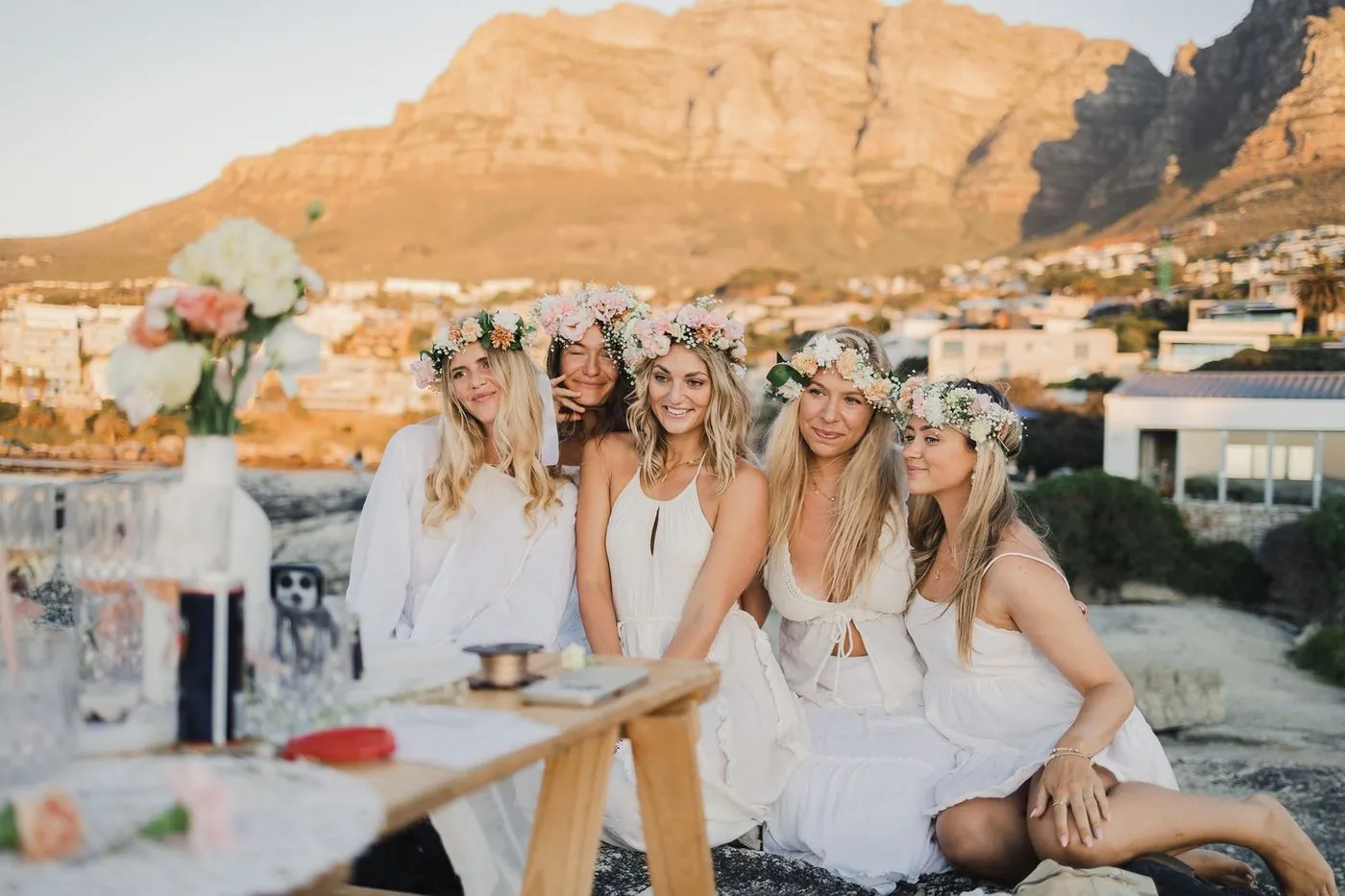 Five friends in floral crowns at a golden-hour flower-crown bachelorette below the Twelve Apostles, Cape Town