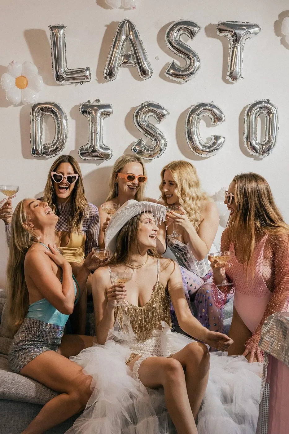 Bridal party in sparkle and swimwear raising coupes under LAST DISCO balloons, the bride in a beaded cowboy hat, Cape Town