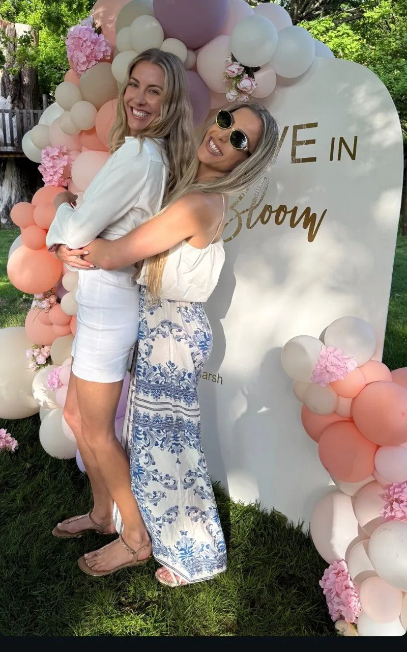 Friends embracing in front of a pastel Love in Bloom balloon arch at a garden celebration