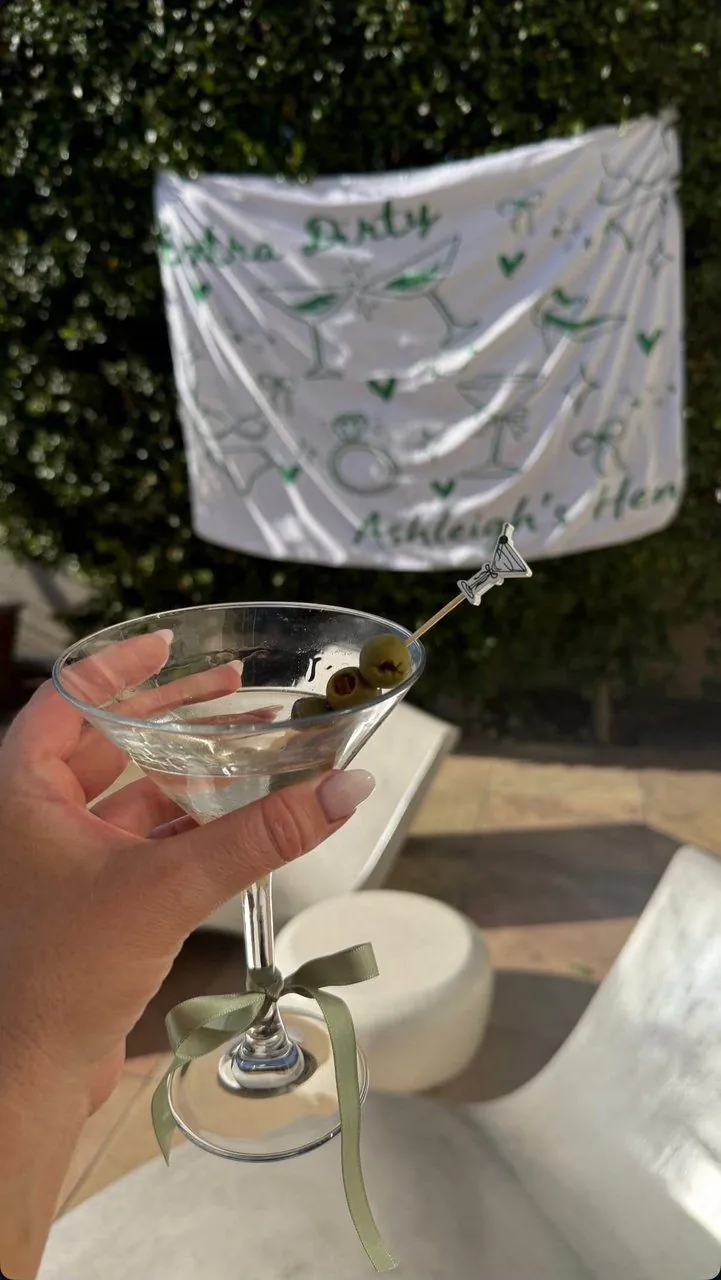 Dirty martini with a sage ribbon bow in front of a personalised hen-party flag