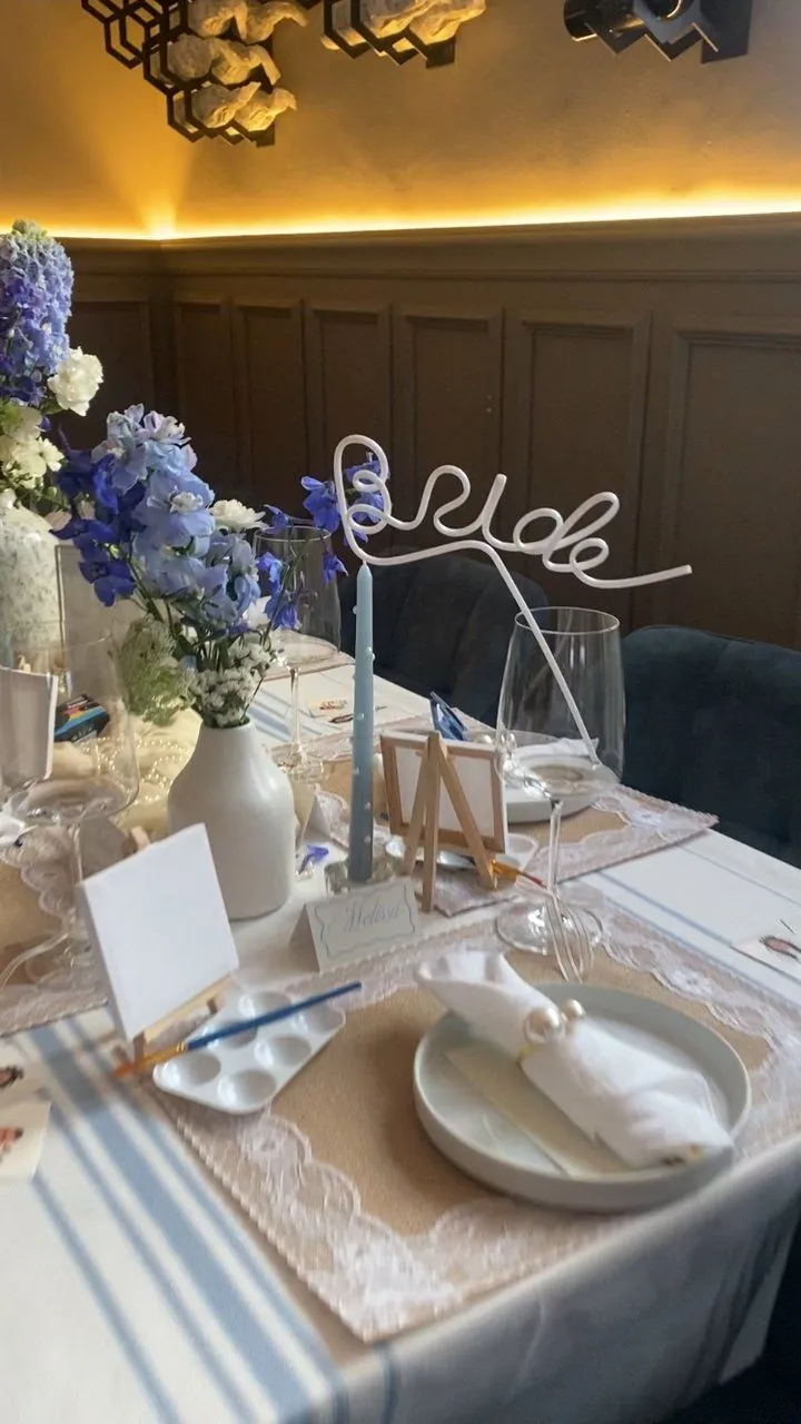 Blue and white paint-and-sip bridal shower tablescape with a wire Bride sign and delphiniums