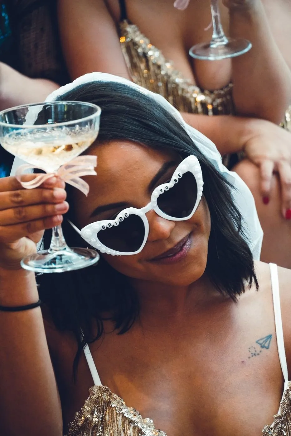 Bride-to-be in a veil and pearl Bride To Be heart sunglasses raising a ribbon-tied coupe at a bachelorette, Cape Town