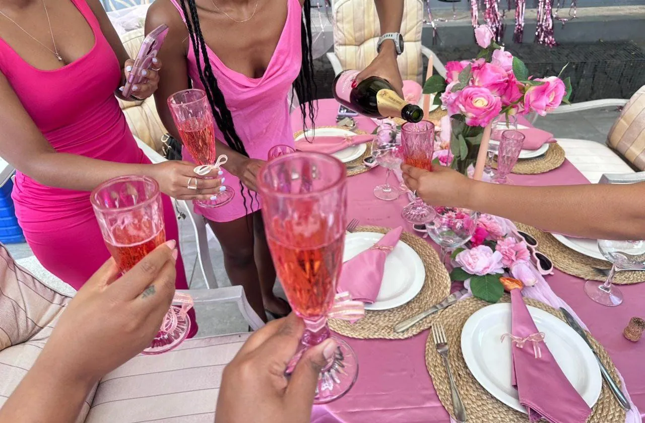 Friends raising pink champagne flutes over a pink rose tablescape at a bachelorette toast