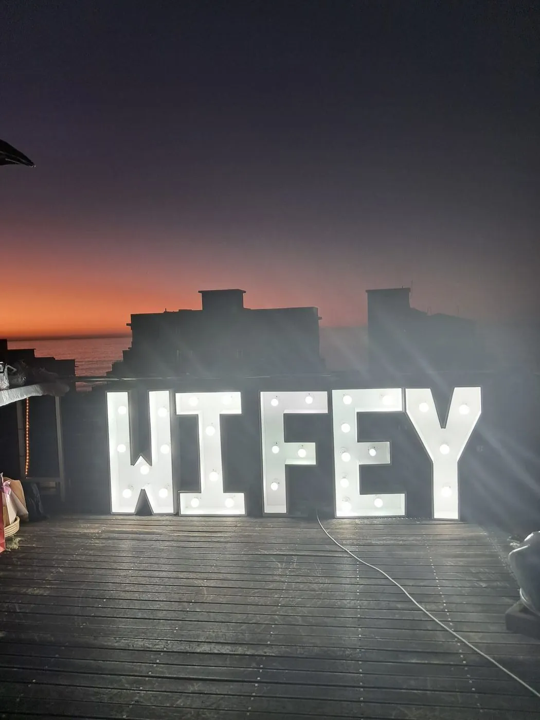 Glowing WIFEY marquee letters overlooking the ocean at sunset on a Sea Point rooftop, Cape Town