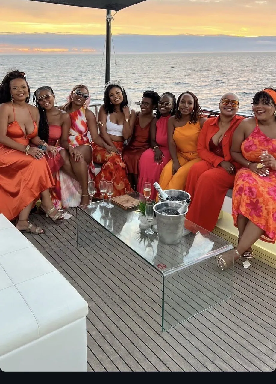 Bachelorette group in orange and coral toasting at sunset aboard a yacht off Cape Town